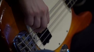 Bas gitar çalan bir adam. Yakın çekim: bir adamın eli dört telli gitarın iplerine dokunur