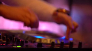 Dj mikser arkasında duruyor, Dj denetleyicisi, müzik karıştırır, kolları büküm, yakın çekim bu büküm çizik, gece kulübü, yapay aydınlatma, ışık müzik mor, sarı, mavi. Gece kulübü partisi