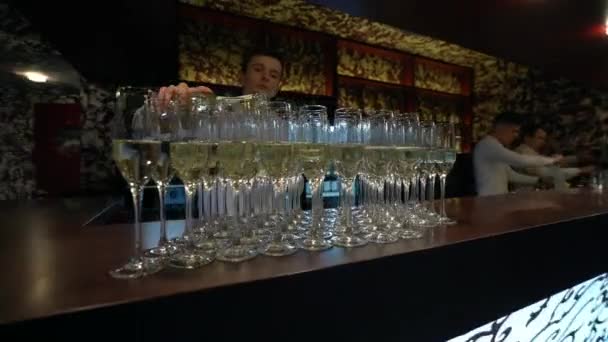 モスクワ ロシア バーにはシャンパンのグラスが多数あるので 白いシャツを着たバーテンダーは空のグラスにボトルからシャンパンを注ぎます — ストック動画