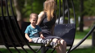 Küçük bir çocuk, bir erkek ile anne, güneşli bir günde ilkbahar veya yaz aylarında Park'ta bir siyah metal salıncak salıncak, kadın uzağa bakar, çocuk diyor, Parkta dinlenme, aile yürüyüşü, ortalama