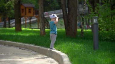 Küçük bebek çocuk yeşil çim yanında kaldırımda yürüyüş, kavak kabartmaetrafında uçan, Park yürümek, Güneşli yaz günü, ortalama planı