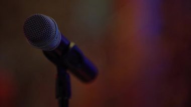 Müzik mikrofonu bir gece kulübünde soldaki siyah bir barda duruyor, yakın çekim, arka planda farklı renklerde geçen insanların siluetleri görebilirsiniz, farklı renklerde yapay aydınlatma