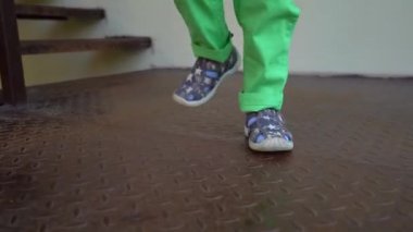 Gri sandalet, mavi çorap ve açık yeşil pantolon metal bir platform üzerinde yürüyen çocuk ayakları, yakın çekim