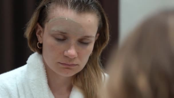 Mulher Europeia Espelho Banheiro Coloca Uma Máscara Facial Para Cuidados — Vídeo de Stock