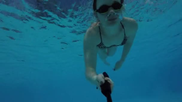 水着と水泳メガネを着たヨーロッパの女性がプールでダイビングし アクションカメラで自分自身を撮影水の下で泳ぐ — ストック動画