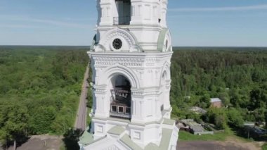 Ortodoks Kilisesi 'nin hava fotoğrafçılığı, kamera beyaz kulenin etrafında saat ve zillerle uçuyor, yaz güneşli bir gün, kırsal kesimde.