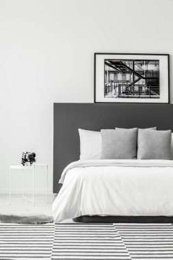 Gri yatak başı en az otel odası iç beyaz masa ile yatağın üzerine siyah poster