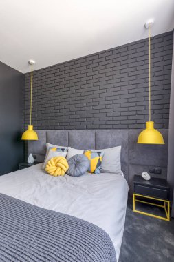 Modern yatak odası iç tuğla duvar ile sarı lambalar arasındaki gri yatak 