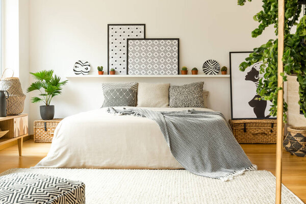 Warm bedroom interior with a comfy bed, patterned blanket and pillows, plants and modern graphics