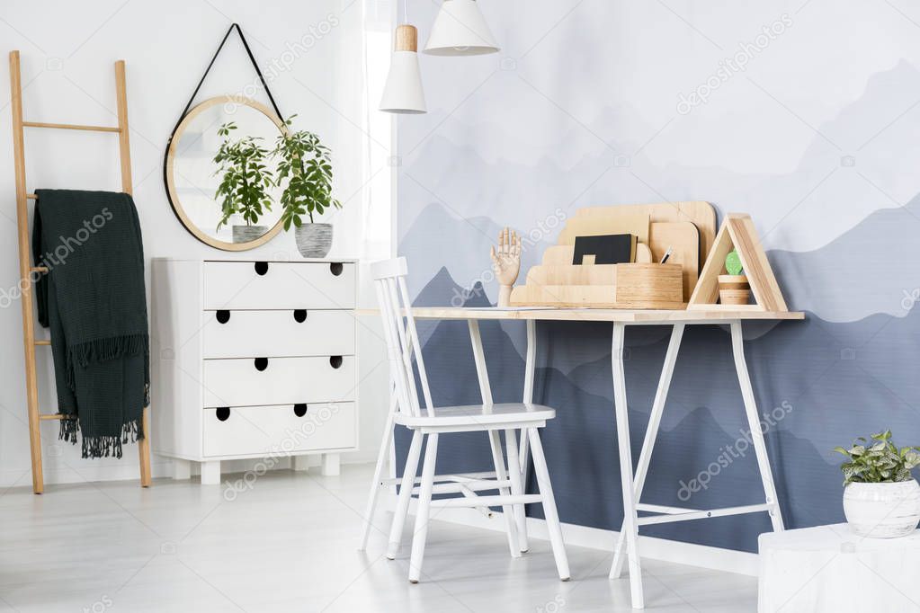 White chair at a desk with wooden organizer standing against the wall with mountain wallpaper in bright home office interior