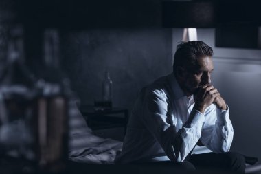 Bir yatakta etrafında alkol duran şişe ile gri bir odada oturup depresyon ile yalnız bir olgun adam portresi