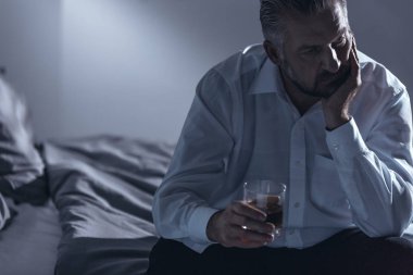 Bir adamın çenesini bir yandan ile bir yatak üzerinde oturan ve bir bardak alkol diğer tutan orta yaş krizi ile yakın çekim