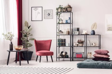 Bir siyah, metal raf aydınlık oturma odası iç kalıplama ile beyaz duvar karşı ayakta süslemeleri ile yanındaki kırmızı, kadife koltuk