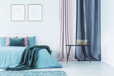 Altın çerçeveler parlak iç perdeler ile çift kişilik yatak ayakta yukarıda duvara asılı iki basit posterler