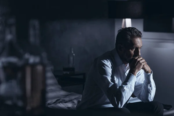 うつ病アルコール突っ立ってのボトルとグレーの部屋でベッドの上に座っている孤独な中年の男性の肖像画 — ストック写真