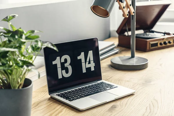 Laptop on a wooden desk, plant, lamp and a vintage record player in a workspace of a bright, hipster living room interior