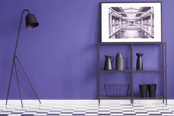 Purple living room with black furniture standing on a checkered floor and a white poster of a factory interior. Real photo