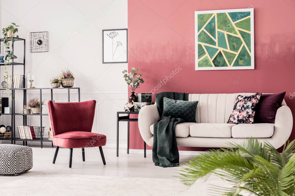 Red armchair next to beige sofa against wall with green painting in cozy living room interior