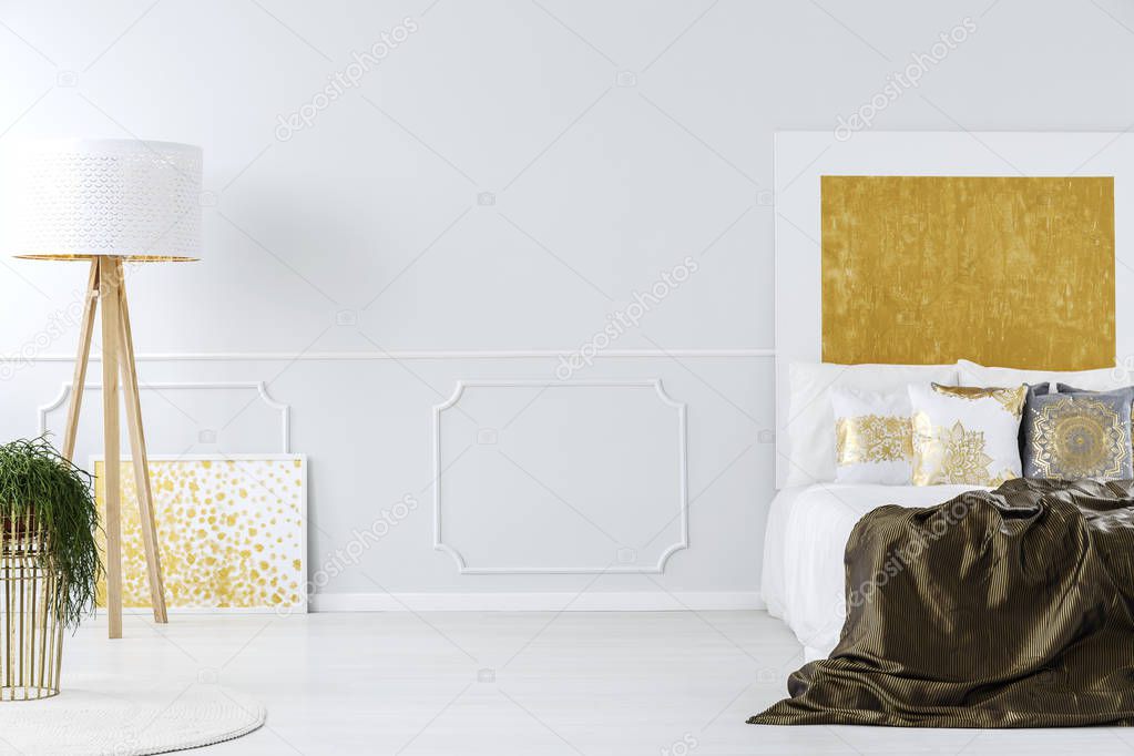 Luxurious white and golden minimalist bedroom interior with elegant furniture and a wooden tripod floor lamp