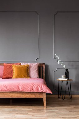 Gri yatak odası iç duvar ve masa kalıp ile pembe ahşap yatakta renkli yastıklar