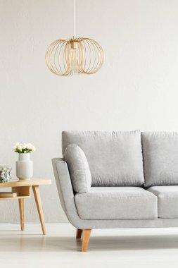 Ahşap bir masa oturma odası iç beyaz çiçeklerle yanındaki gri kanepe üzerinde altın lamba