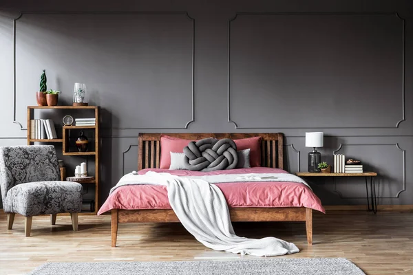 花纹扶手椅旁边的木床与粉红色床上用品和白色毯子在老式卧室内饰 — 图库照片