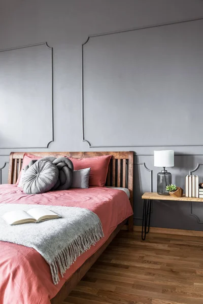 居心地の良いベッドルームのインテリアで成形で灰色の壁に木製のピンクのベッドの上の毛布に予約します — ストック写真
