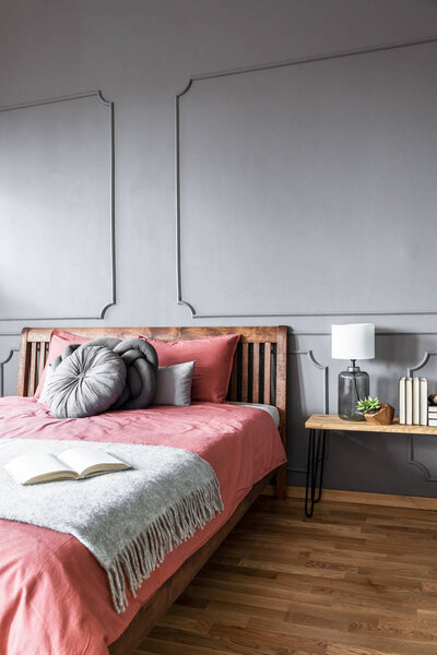Book on blanket on wooden pink bed against grey wall with molding in cozy bedroom interior
