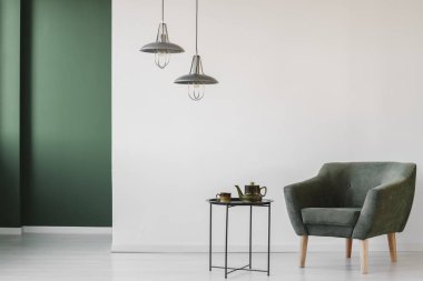 Döşemeli, karanlık koltuk ve bir çaydanlık ve minimalist oturma odası iç yeşil köşe ile Kupası ile bir sanayi yan sehpa