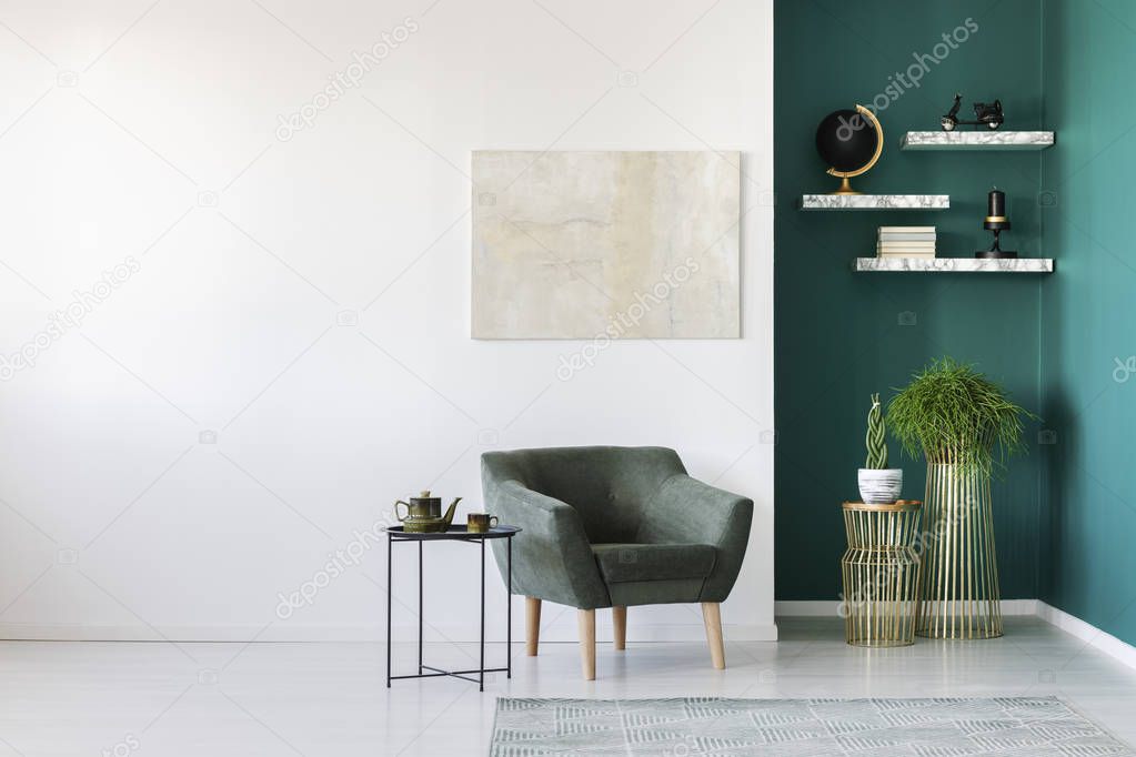 Simple living room interior with green armchair, plants, teapot set on the table and marble shelves on the wall