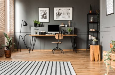 Gri çalışma alanı iç posterler ile bilgisayar monitörü ile tablo yakınındaki ahşap dışkı üzerinde bitki