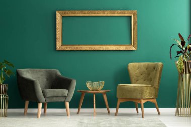 Altın çerçeve yeşil iç iki koltuk ve ahşap masa üzerinde dekoratif kase ile duvara asılı