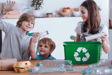Gülümseyen çocuklar eğleniyor plastik şişeler ve kağıt yeşil bir depo gözüne yavru iken