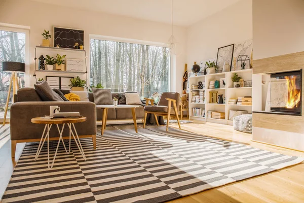 Nordic style living room interior with striped carpet, corner couch with pillows, fireplace, big window and library on white rack