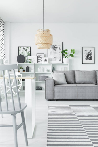 Art collection in a white living room interior with a grey sofa, chair and beige chandelier