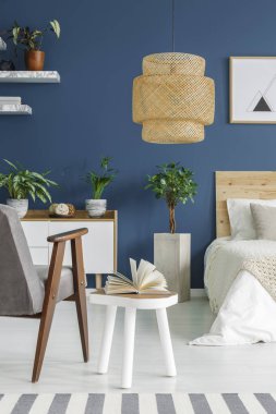 Mavi yatak odası iç büyük hasır lamba, beyaz dolap ve sehpa üzerinde açık kitap ile taze saksı bitkileri