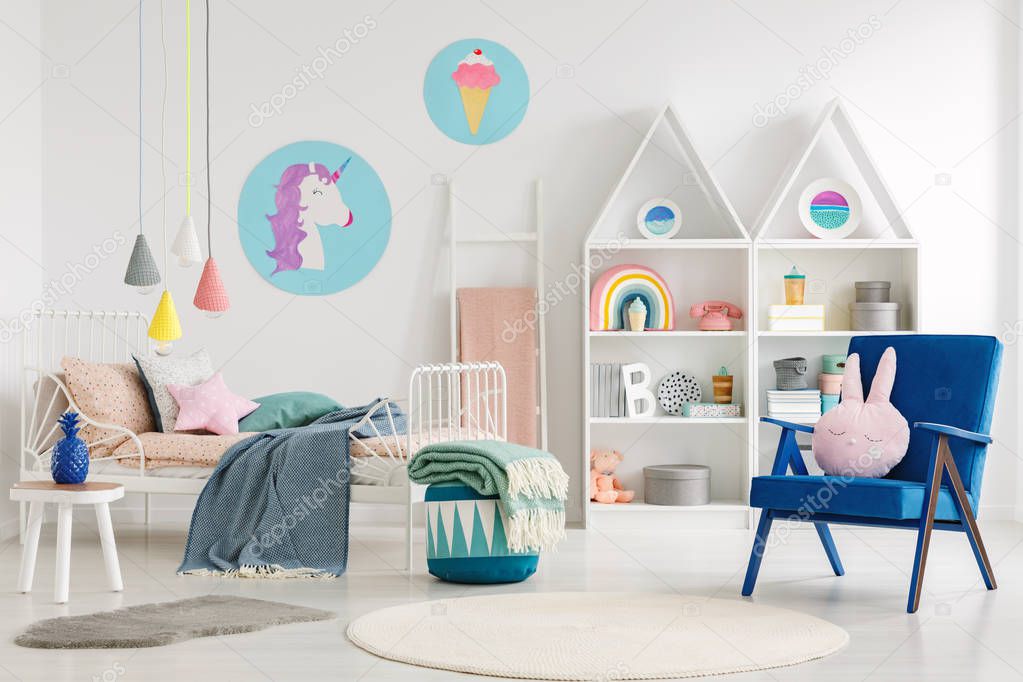 Sweet bedroom interior for a kid with a blue armchair, rabbit pillow, bed, unicorn, ice-cream posters and shelves