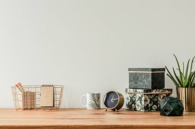 Organize masa üstü çiçek kutuları, kupa, saat ve metal kutusu boş bir duvar ile