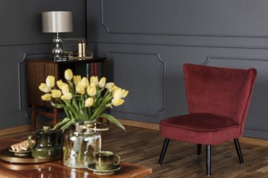 Kırmızı koltukta koyu gri oturma odası iç bulanık ön planda masaya lamba ve sarı çiçek ile