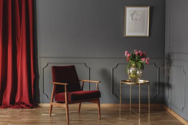 Çiçekli salon iç posteri ile altın tablosunun yanındaki kırmızı ahşap tekli