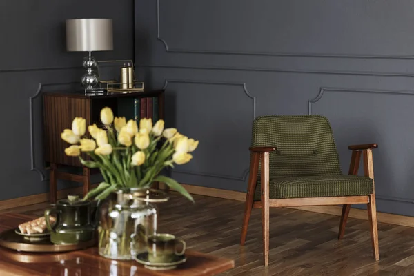 真实照片的绿色 老式的扶手椅在客厅内部与一个木橱柜在背景和模糊的黄色郁金香在前景 — 图库照片