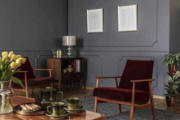 Плакаты на серой стене с лепкой в интерьере гостиной с красным деревянным креслом
