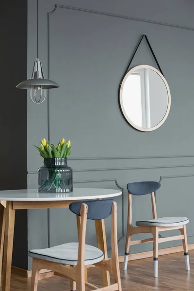 Round mirror on a grey wall and wooden table with chairs in a dining area