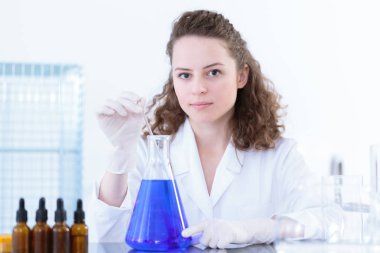 Test sırasında ilaç tıp bir cam çubuk ile bir laboratuvar şişesi içinde mavi bir karışımı karıştırma kadın bilim adamı