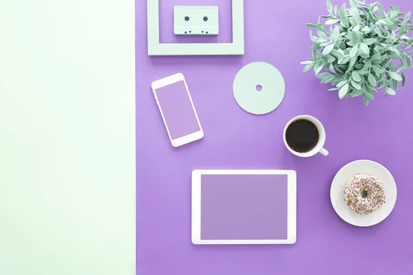 Mockup of freelancer's smartphone and tablet on ultra violet desk with cup of coffee and doughnut