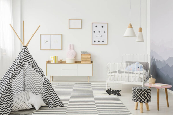 Patterned tent near stool in child's bedroom interior with posters on white wall above wooden cupboard