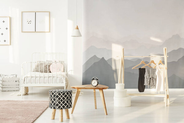 Sun shining on a landscape wallpaper of a stylish little girl's bedroom interior with clothes on a creative and functional wooden hanger