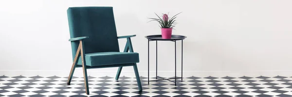 Green armchair and metal end table with fresh plant in pink pot standing in white room interior with place for your chair
