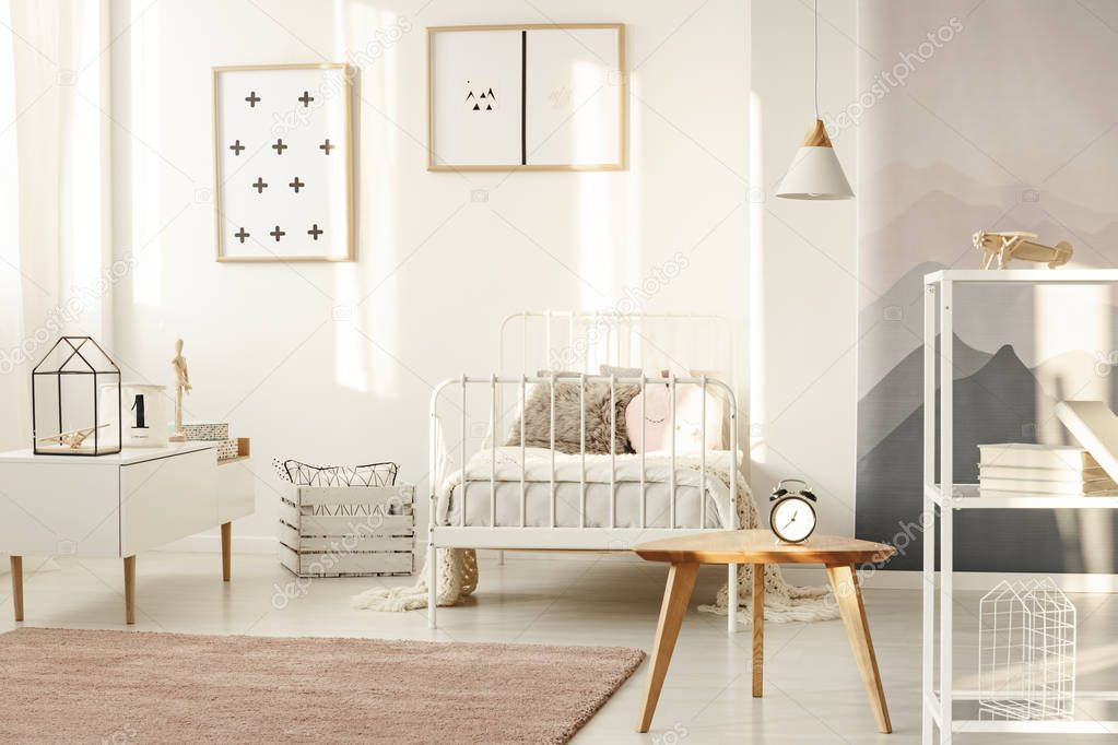 Clock on wooden table in girl's bedroom interior with posters on white wall and pink carpet