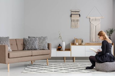 DIY dekor ile modern oturma odası iç kahverengi kanepe yakınındaki desenli kabarık kadın. Gerçek fotoğraf